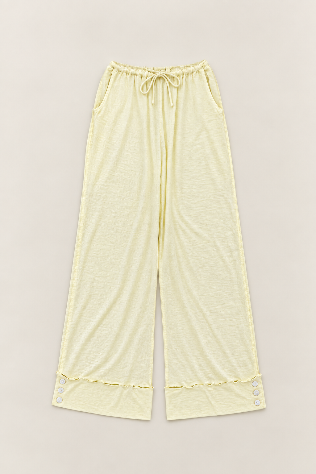 Light yellow wide-leg lounge pants with an elastic drawstring waistband and decorative button trim at the hems, shown flat on a light beige background.