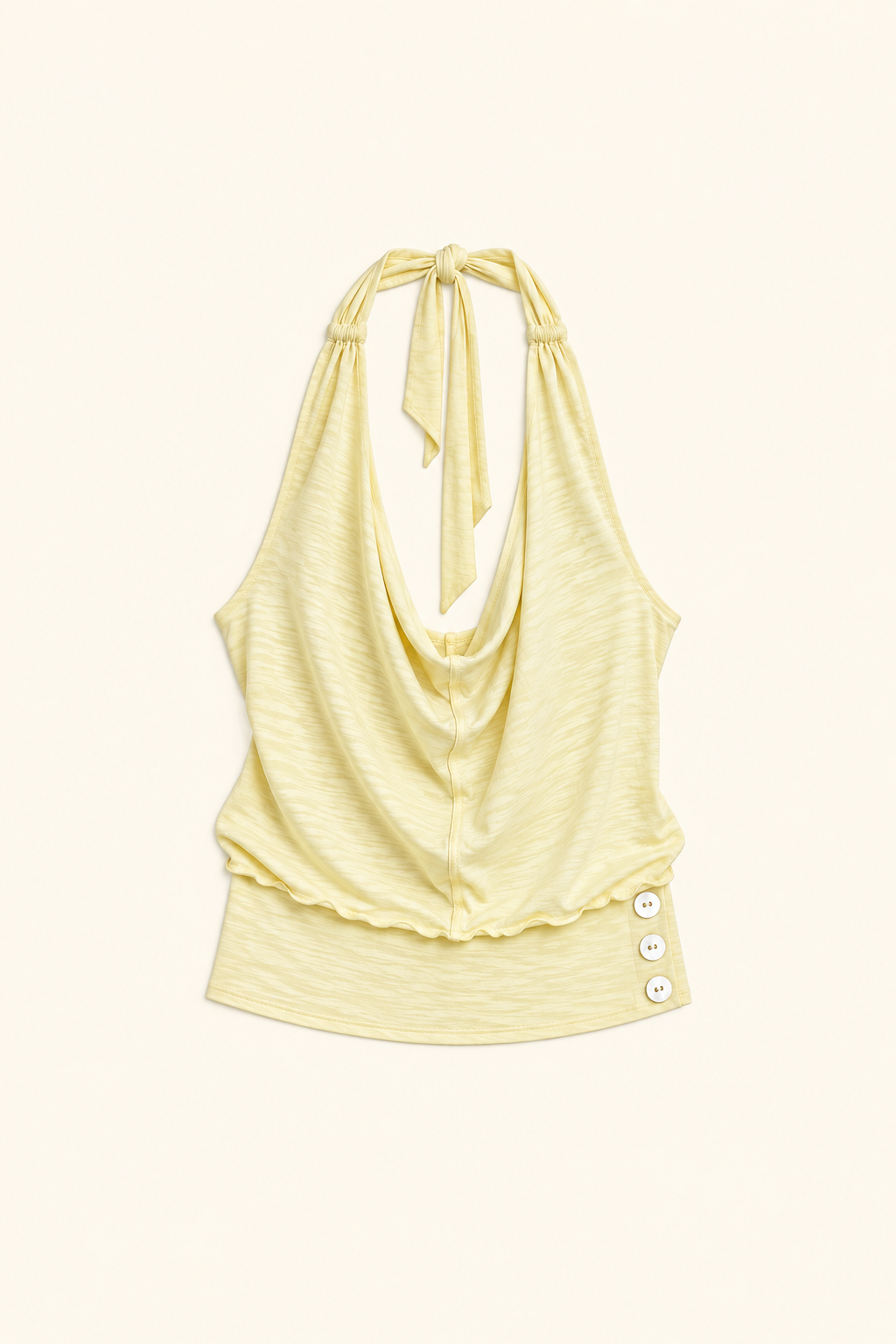 A pale yellow halter top with a draped cowl neckline, tie-back straps, and three decorative buttons on the side, displayed flat against a light cream background.