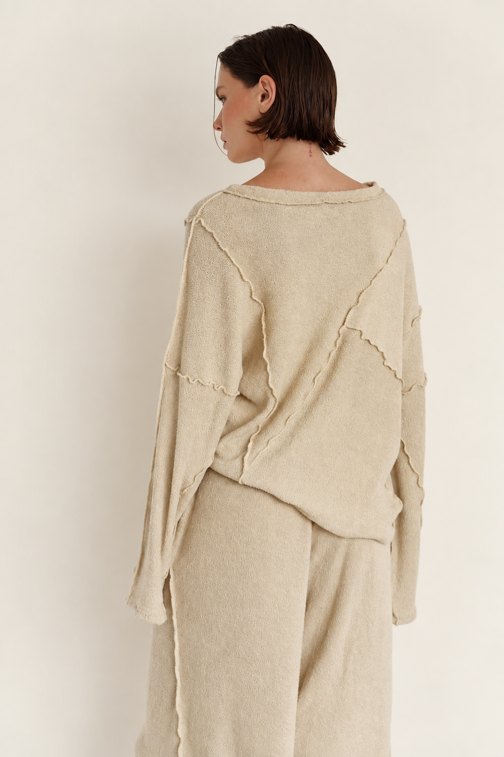 Woman standing with her back to the camera wearing a cream knitted set with  seams running through the sweater. 