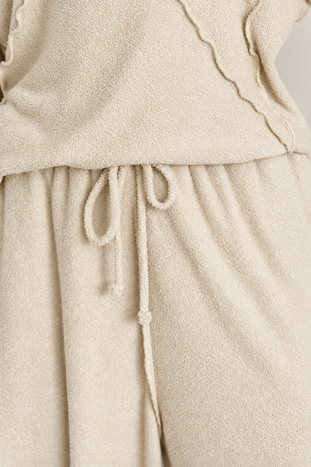 Close-up of a cream-colored textured fleece or terry cloth garment, showing a drawstring waist and soft fabric folds.