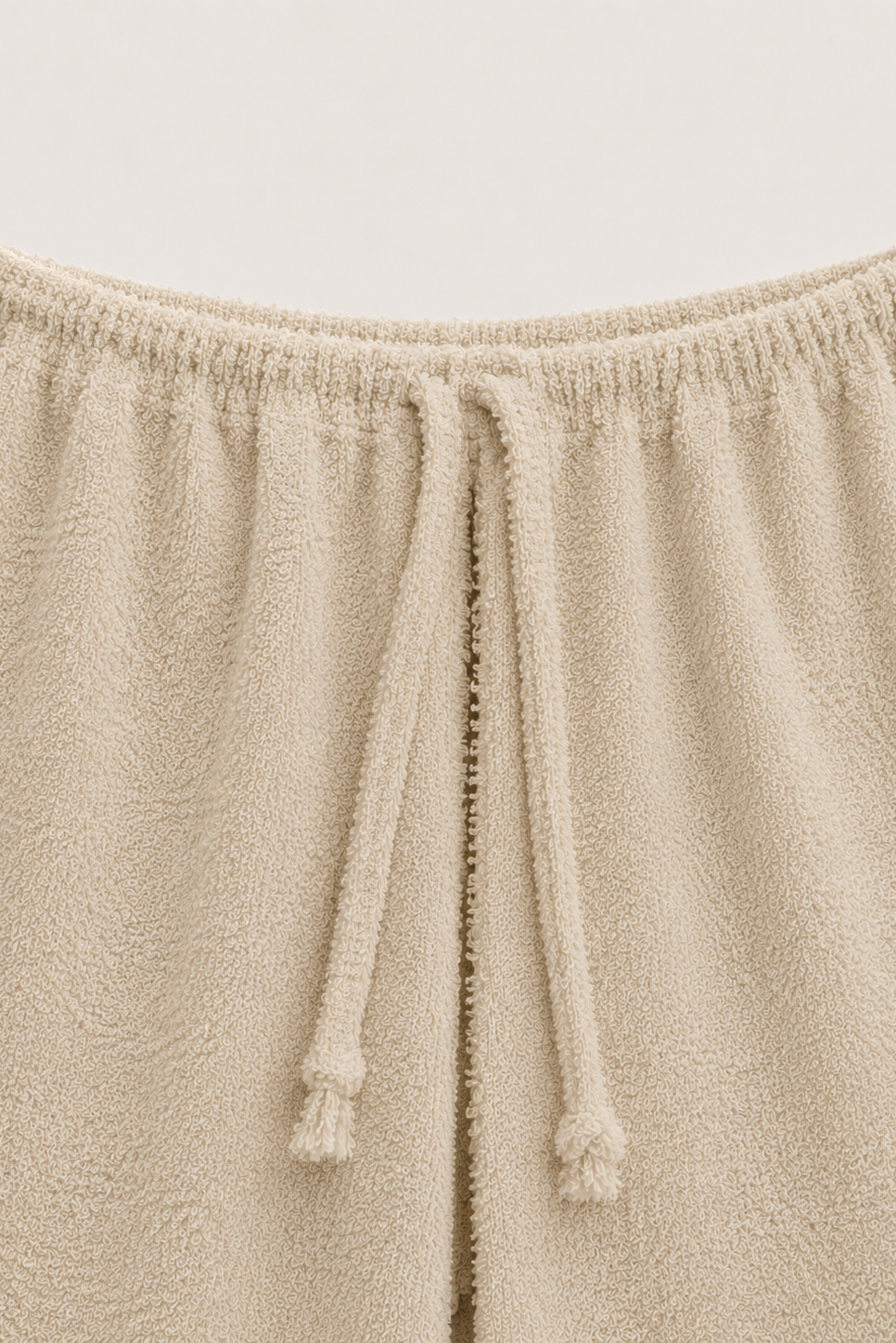 Close-up of a beige textured lounge pants fabric with an elastic waistband and matching drawstring.