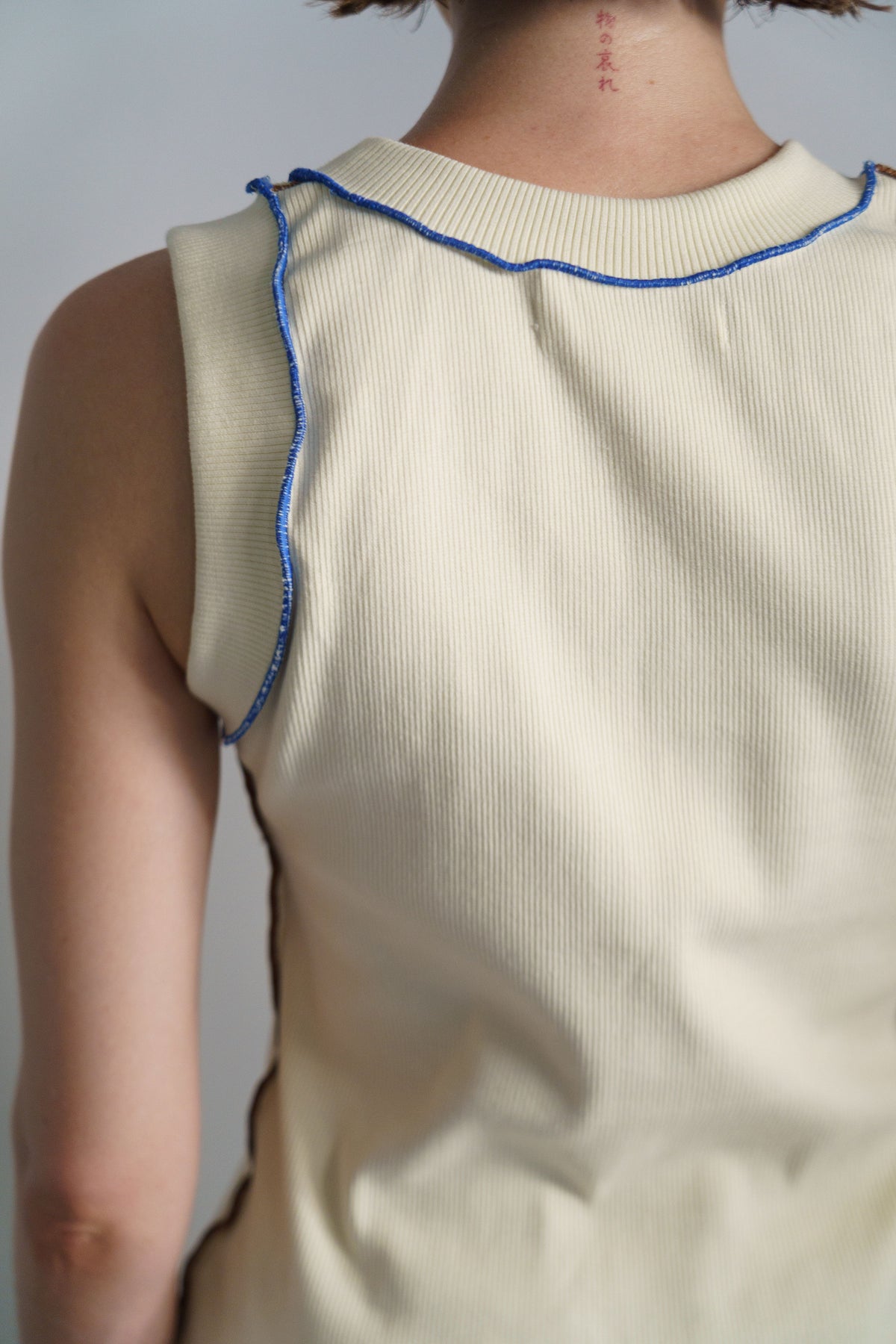 Close-up back view of a person wearing a ribbed cream sleeveless top with blue trim along the neckline and armholes.