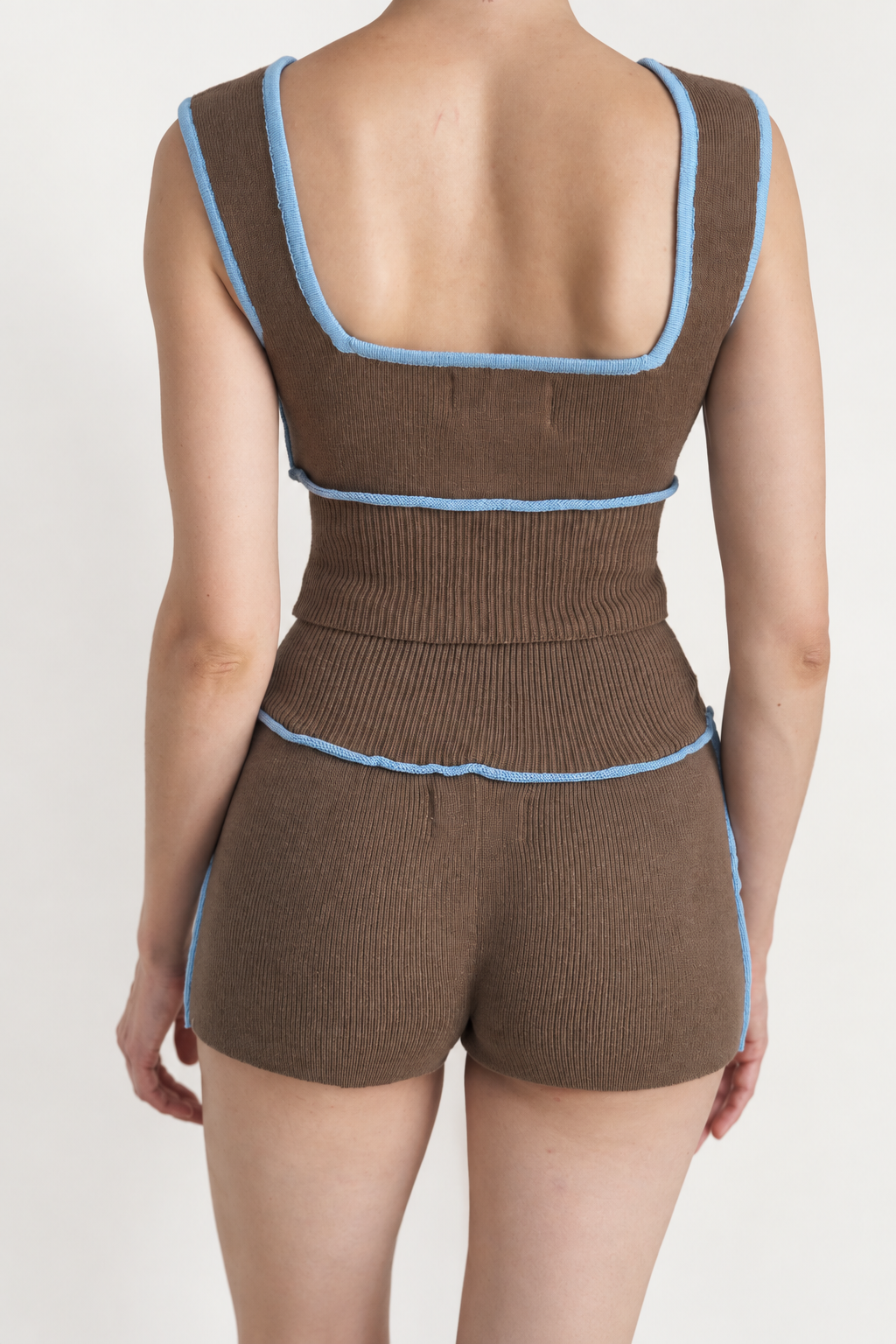A model shown from the back wearing a brown ribbed knit romper with light blue trim details, set against a plain light background.