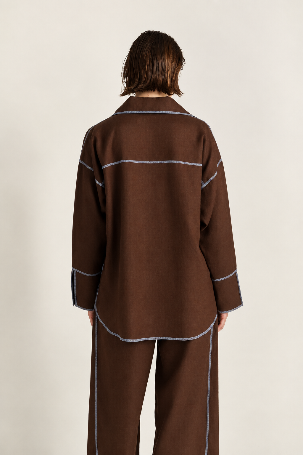 A model viewed from the back wearing a brown long-sleeve shirt and matching pants with light blue contrast stitching, set against a plain off-white background.