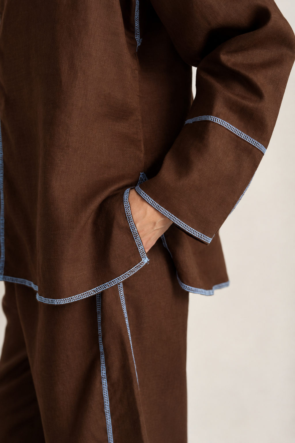 A close-up of a person wearing a brown pajama set with light blue patterned piping along the edges of the top and pants.